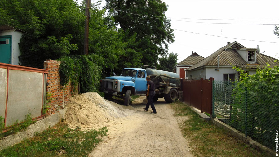 Вантажівка асенізатору ГАЗ намагається заїхати задом на подвір'я з вузького провулку. Богуслав