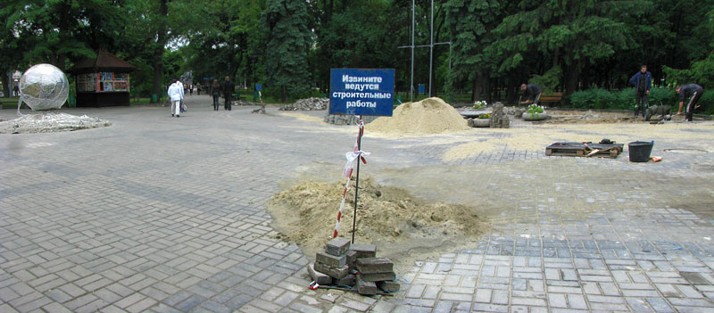 Робочі перекладають плитку біля пам'ятнику футбольному м'ячу в целофані. Харків, Україна 