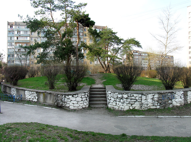 ступеньки и каменная оградка холма во дворе в Украинке. Скамейка на холме