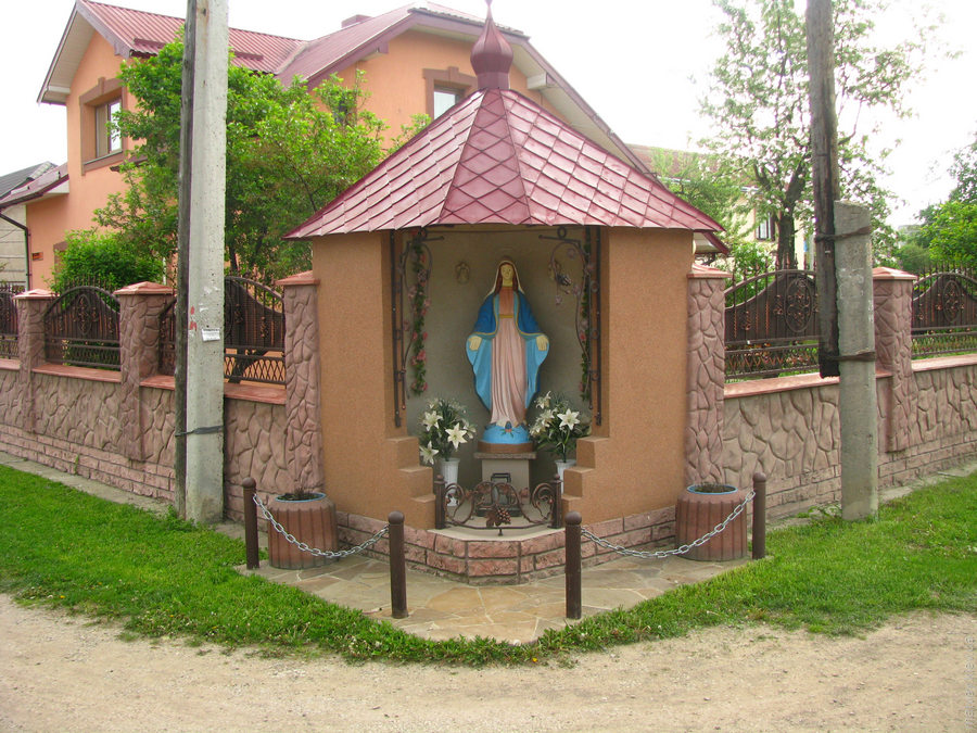 Угловая статуя девы Марии с клумбами и цветами в заборе частного дома