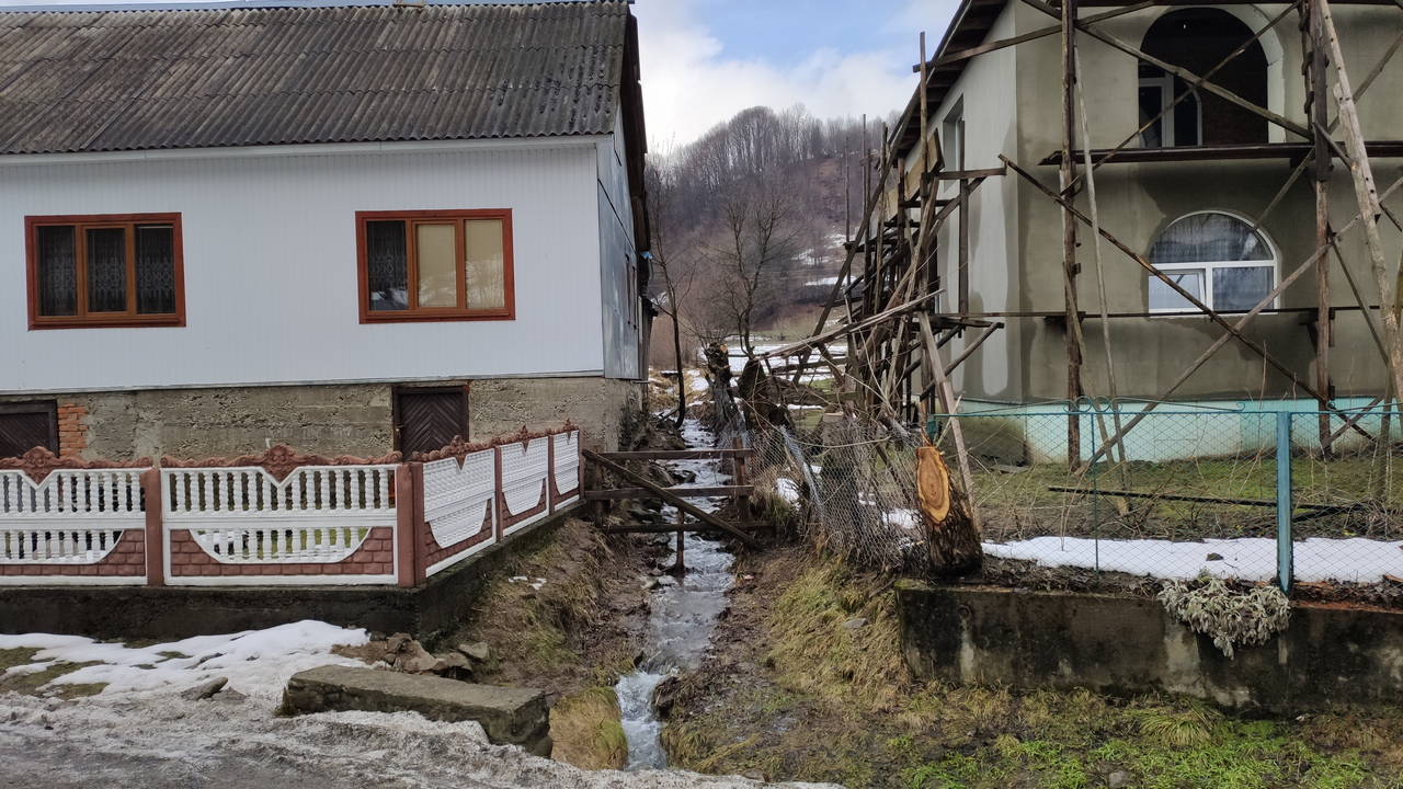 Струмок тече між будинками. Колочава, Карпати, Україна